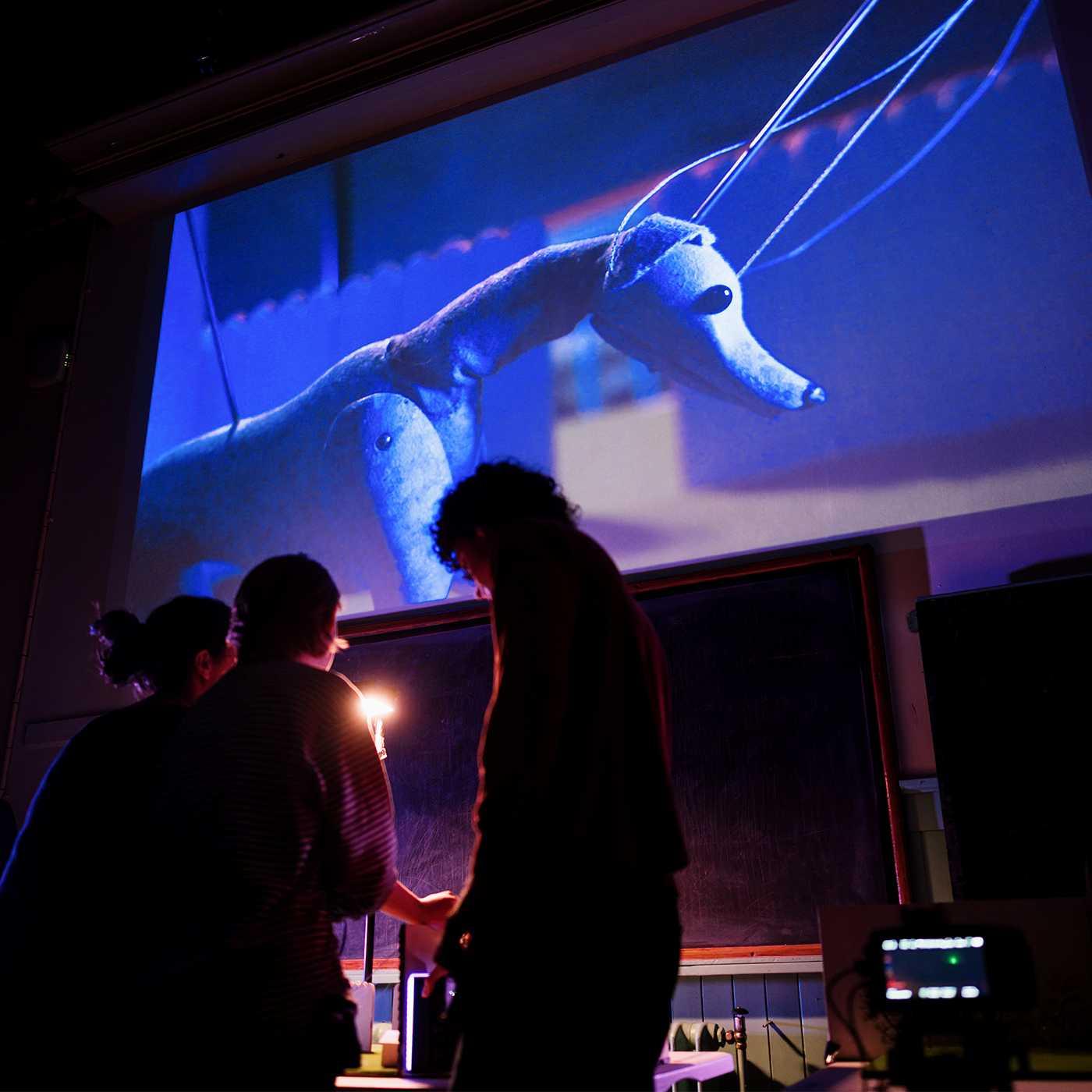 A puppet dog on a big screen and people watching