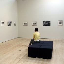 An image of somebody sitting in an art gallery, looking at small black and white art pieces