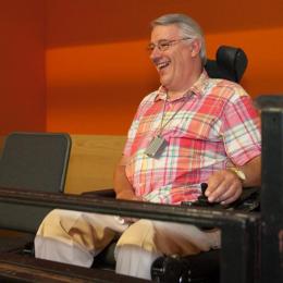 A man using a wheelchair smiles whilst sitting in the auditorium